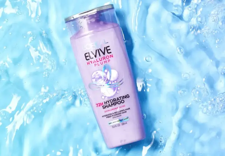 Botella de champú Elvive Hyaluron Plump sobre fondo azul con burbujas, ideal para pelo seco.