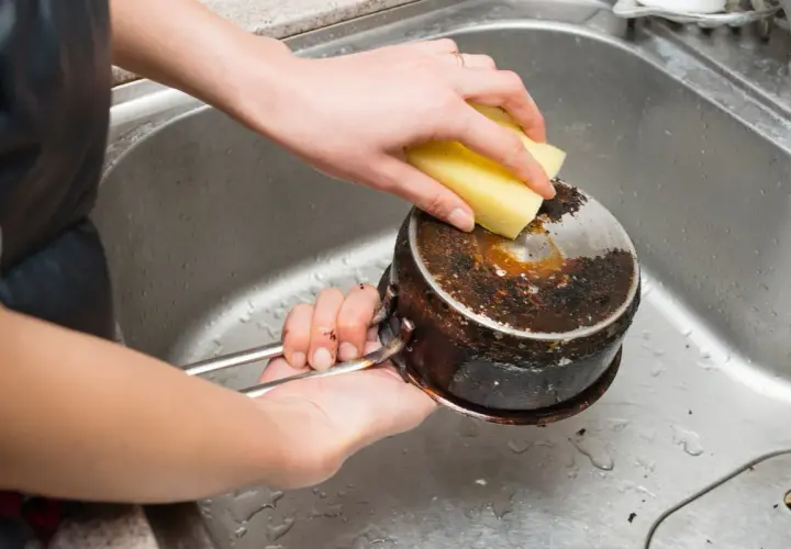 Nettoyage d'une casserole brûlée avec une éponge. Le bicarbonate de soude sera utile pour cette tâche difficile.