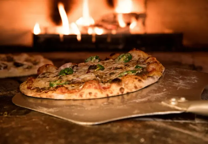 Pizza z pomidorami z puszki, serem i papryczkami jalapeno na łopacie, w tle płomienie pieca.