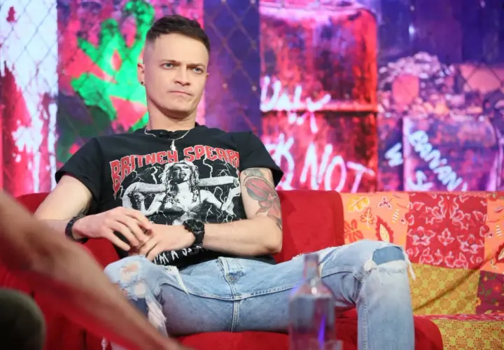 Nocny kochanek wokalista w czarnej koszulce z Britney Spears, siedzi na kanapie w podartych jeansach.