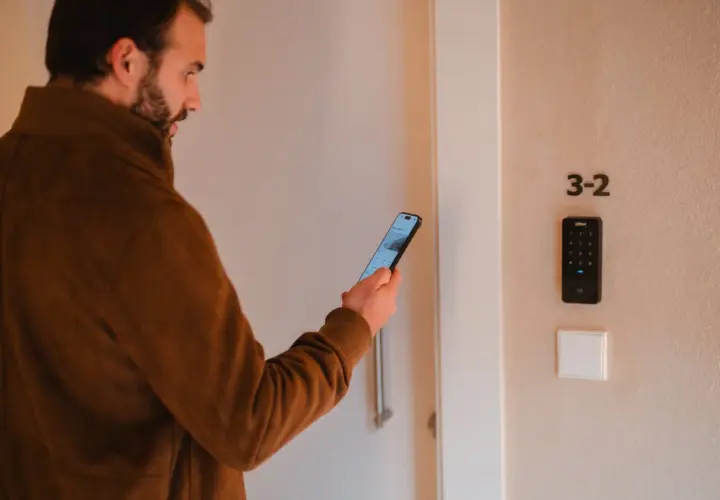Hombre con móvil frente a puerta con teclado numérico. Una de las desventajas de la domótica es la dependencia tecnológica.