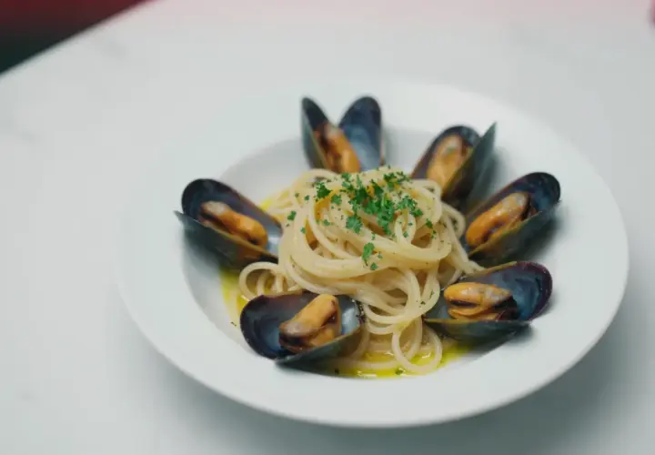 Spaghetti z małżami, danie pełne smaku morza, ozdobione świeżą natką pietruszki.