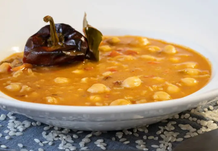 Un plato de garbanzos con arroz, con un pimiento seco y una hoja de laurel encima.