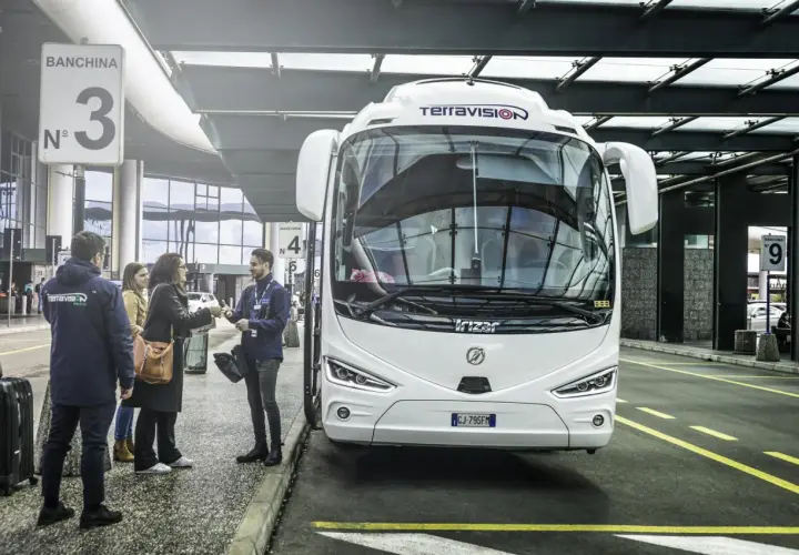Autobus Terravision czeka na pasażerów na jednym z mediolan lotniska. Ludzie z bagażami rozmawiają z pracownikiem.
