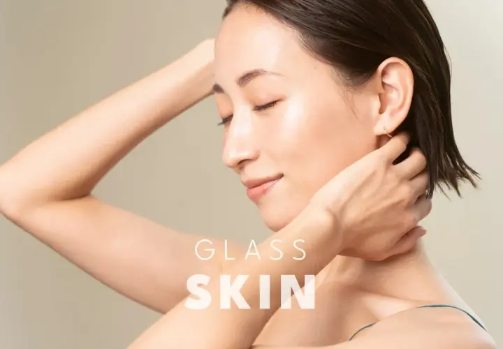Kobieta z idealną, lśniącą cerą typu "glass skin", z dłońmi na karku.