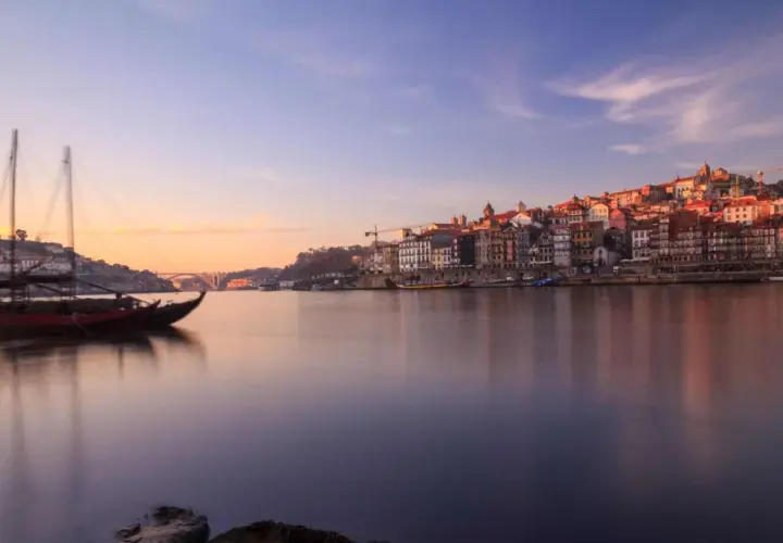 Barcos tradicionales navegan por el río Duero al amanecer, con la pintoresca ciudad de Oporto al fondo. Un lugar imprescindible que ver en el norte de Portugal.