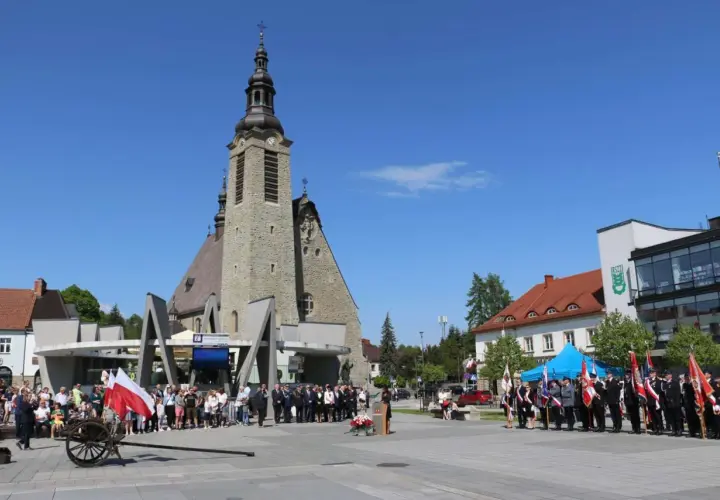 Uroczystość przed kościołem w Limanowej. Ludzie, delegacje w mundurach i polskie flagi.