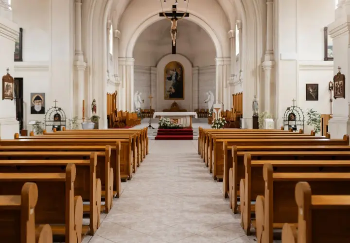 Wnętrze kościoła z rzędami drewnianych ławek. W ołtarzu głównym wisi obraz, a nad nim krucyfiks. 1 maja święto kościelne, czas zadumy.