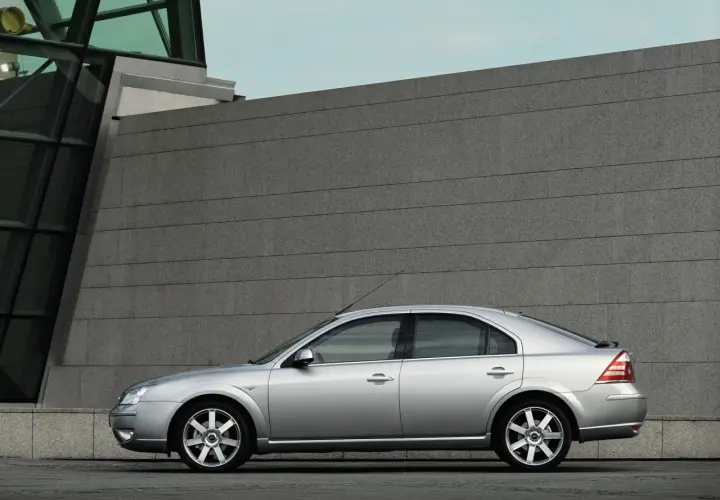 Srebrny Ford Mondeo MK3 2.0 TDCI stoi na tle nowoczesnego budynku z kamienną fasadą.