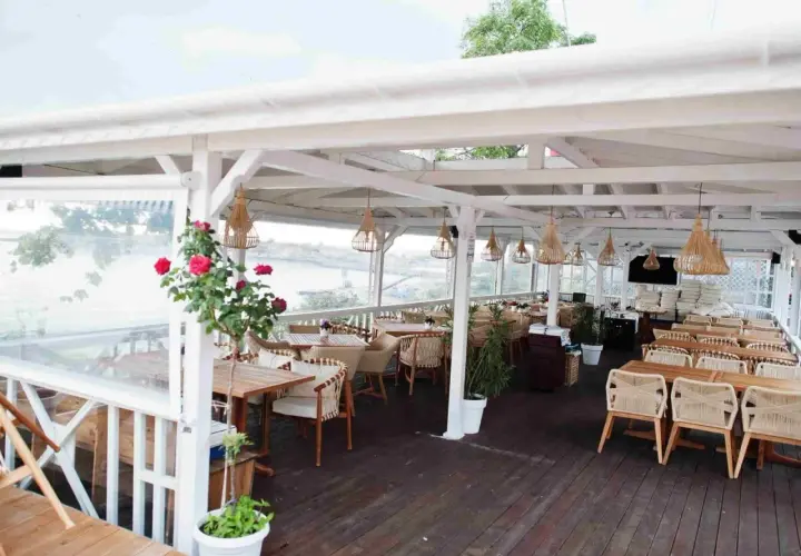 Letnia restauracja z widokiem na wodę. Krzesła i stoły z rattanu, wiszące lampy. Idealne miejsce na pyszne jurata jedzenie.