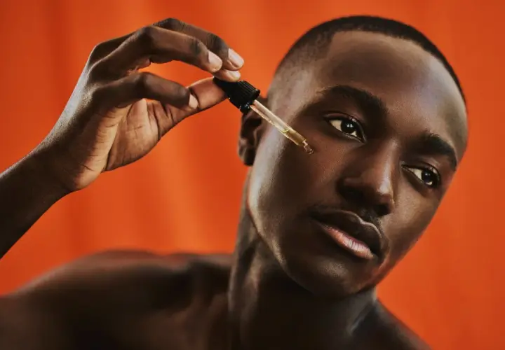 Uomo con pelle scura applica un siero con contagocce, parte della sua beauty routine viso.