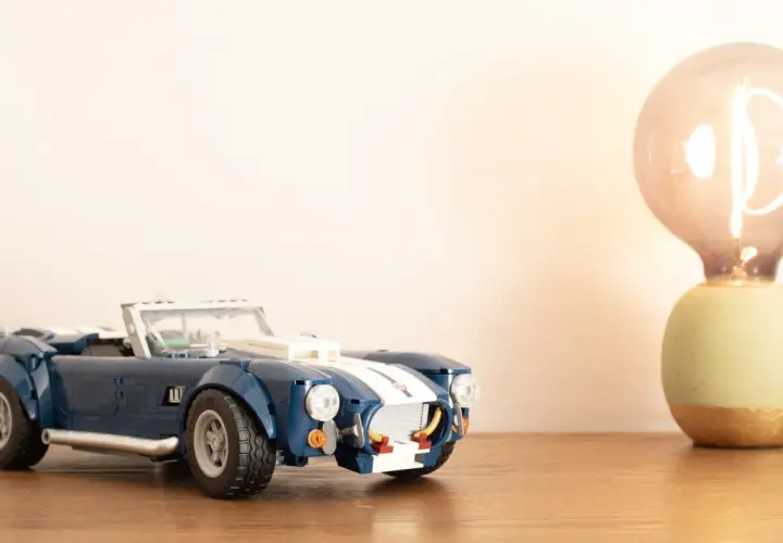 Ein blauer Lego Shelby Cobra steht neben einer leuchtenden Glühbirne.