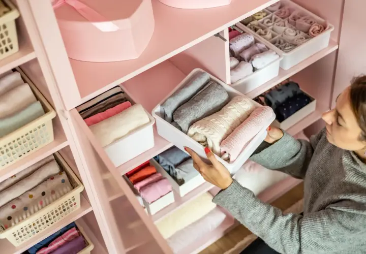 Frau sortiert Kleidung in einem rosa Kleiderschrank. So organisiere ich meinen Kleiderschrank: gefaltete Pullover und Socken in Behältern.