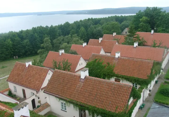 Urokliwe, pokryte czerwonymi dachówkami domy w Sejnach, otoczone zielenią, z widokiem na jezioro. Atrakcje regionu.