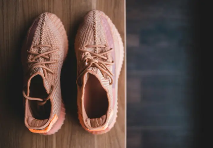 Pomarańczowe sneakersy z plecionki, idealne na szeroką stopę, leżą na drewnianym blacie.