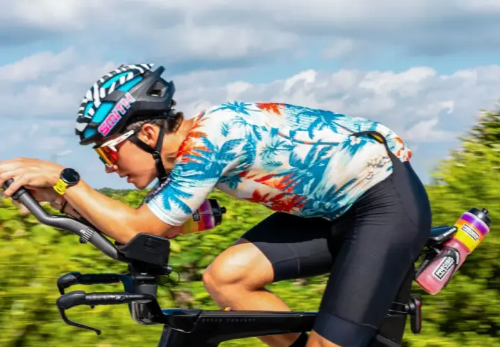 Ciclista en Mallorca en bici, con casco y gafas, pedaleando con fuerza en un día soleado.