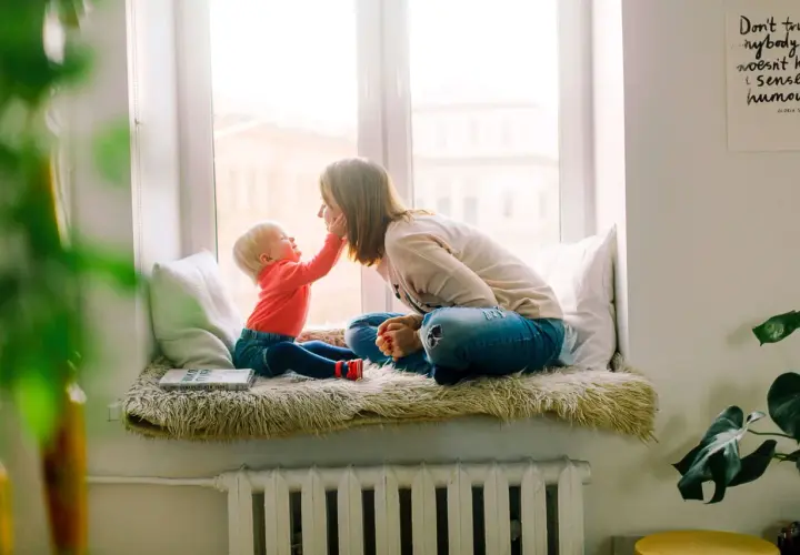 Mama i dziecko siedzą na parapecie. Wzór umowy najmu mieszkania dla rodziny z dzieckiem jest na książce.
