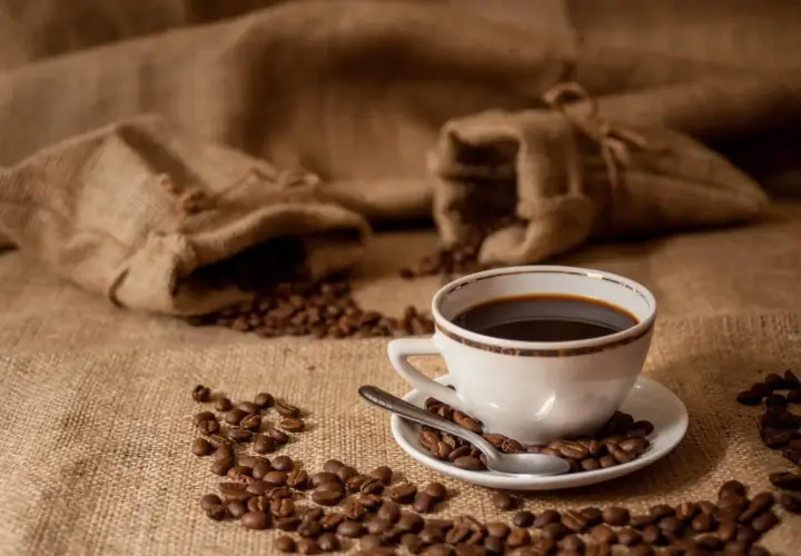 Aromatic coffee beans spill from burlap sacks, surrounding a white cup of dark brew. Zastanawiasz się, ile kofeiny ma kawa parzona?