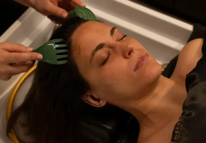 Relajante masaje capilar en un spa. Herramientas verdes estimulan el cuero cabelludo para un tratamiento de spa cabello revitalizante.