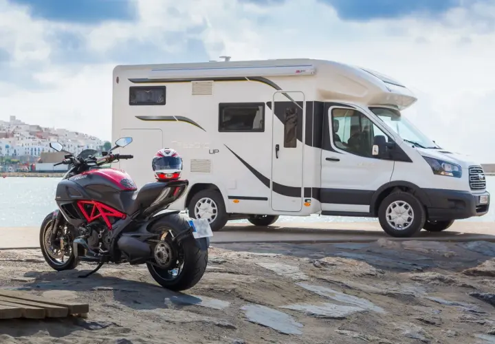 Un camping-car et une moto sportive Ducati sont garés près de la mer, prêts pour une aventure.