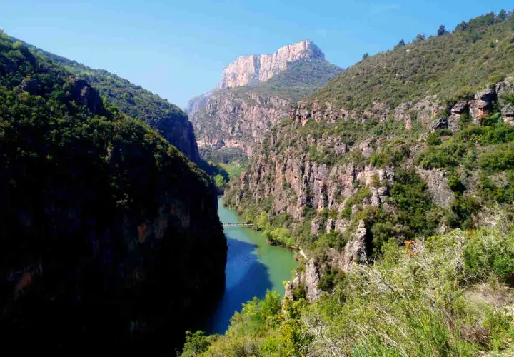 El río serpentea entre imponentes paredes rocosas en el congost del Mu, coronado por un pico montañoso.