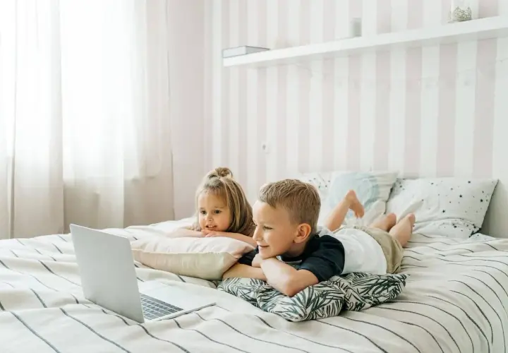 Dzieci leżą na łóżku, oglądając edukacyjne bajki dla dzieci na laptopie.
