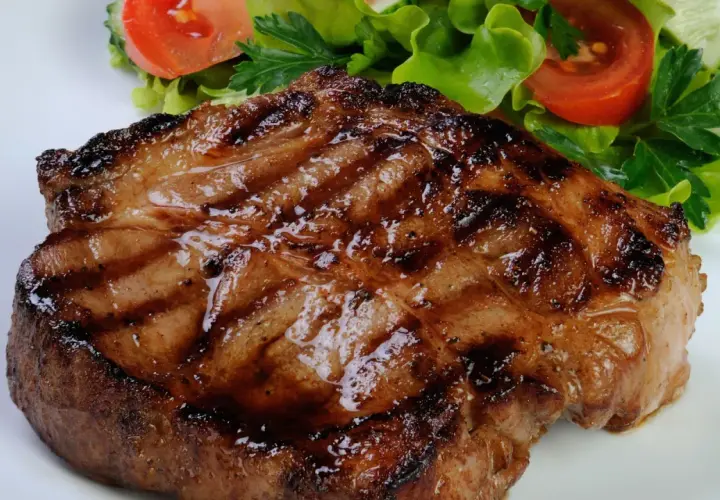 Bistecca di maiale succulenta e grigliata, servita con un'insalata fresca di lattuga, pomodoro e cetriolo.