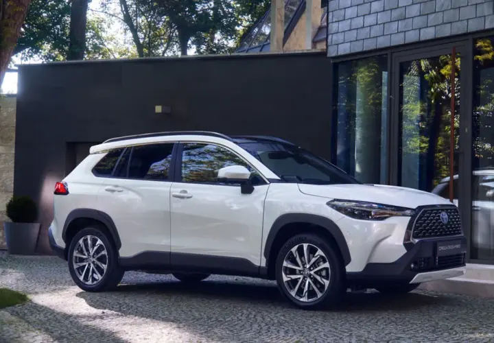 Biała Toyota Corolla Cross zaparkowana przed nowoczesnym budynkiem. Sprawdź jej wymiary, by poznać jej kompaktową sylwetkę.