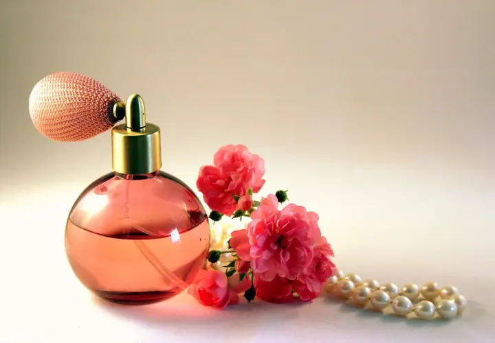 Frasco de perfume rosa con atomizador, rosas rosadas y collar de perlas. Un aroma que evoca la dulzura del almizcle que es.