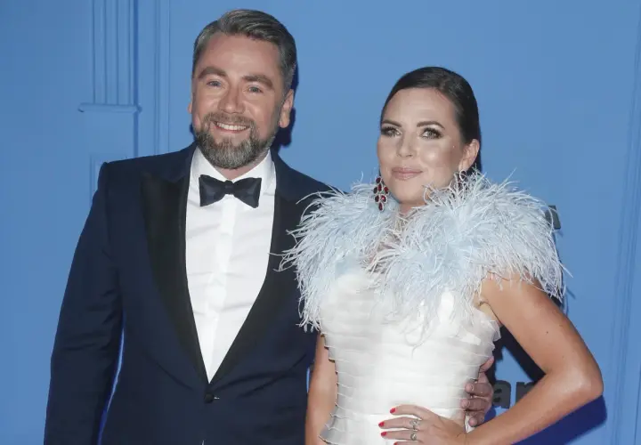 Mąż Oli Kwaśniewskiej, Piotr, w eleganckim smokingu u boku żony w białej sukni z piórami.