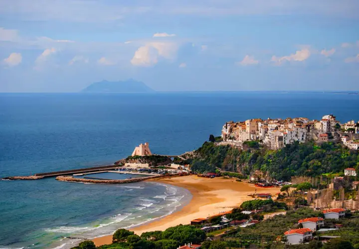 Vue d'un village pittoresque perché sur une falaise surplombant la mer, avec une plage de sable et un port. On dirait un **ostie** de **Rome** !