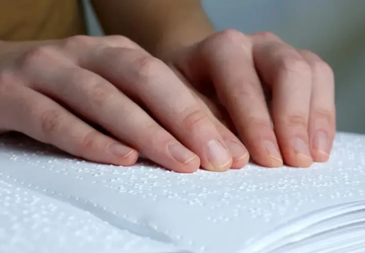 Dłonie osoby czytającej książkę w alfabecie Braille'a.