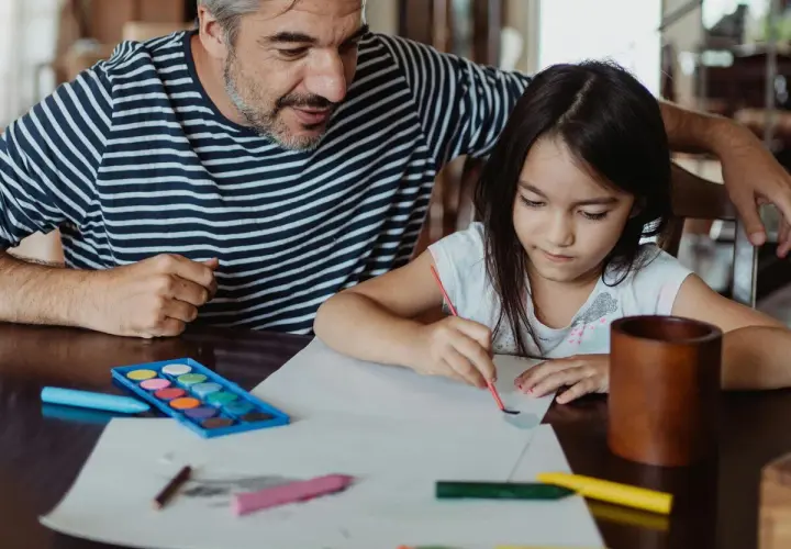 Padre e hija pintando con acuarelas y lápices de colores. Un momento de creatividad con materiales de escuela infantil.
