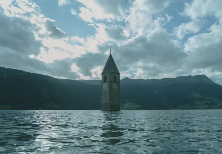 Torre sommersa nel lago, un'icona di Curon. Le recensioni la descrivono come un luogo suggestivo e malinconico, con montagne sullo sfondo.
