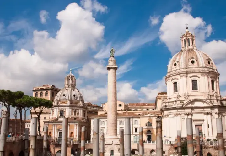 La colonna di Traiano si erge maestosa a Roma, con cupole barocche e pini marittimi sotto un cielo azzurro e nuvoloso.