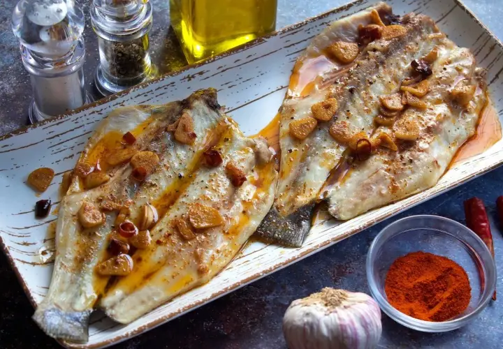 Dos filetes de lubina a la bilbaina, dorados y jugosos, con láminas de ajo y guindilla, listos para disfrutar.