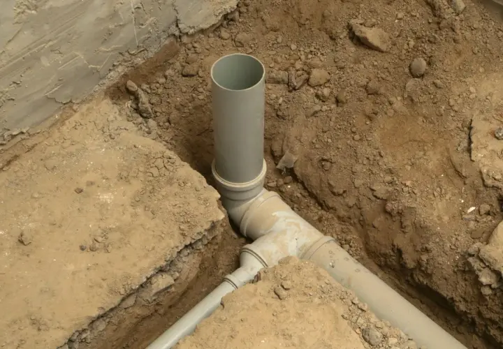 Instalacja kanalizacyjna w domu w trakcie budowy. Szare rury PVC połączone w wykopie ziemnym.