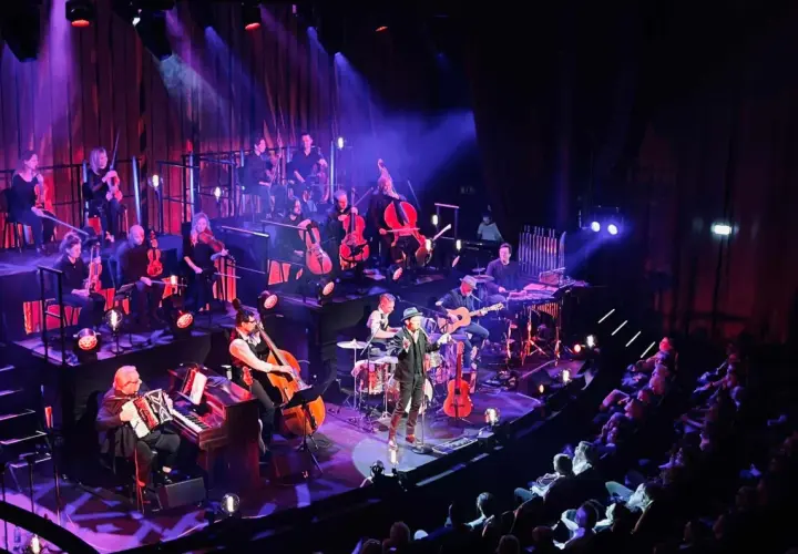 En orkester spelar på en scen i Stockholm, med en sångare i förgrunden. En levande revyupplevelse.