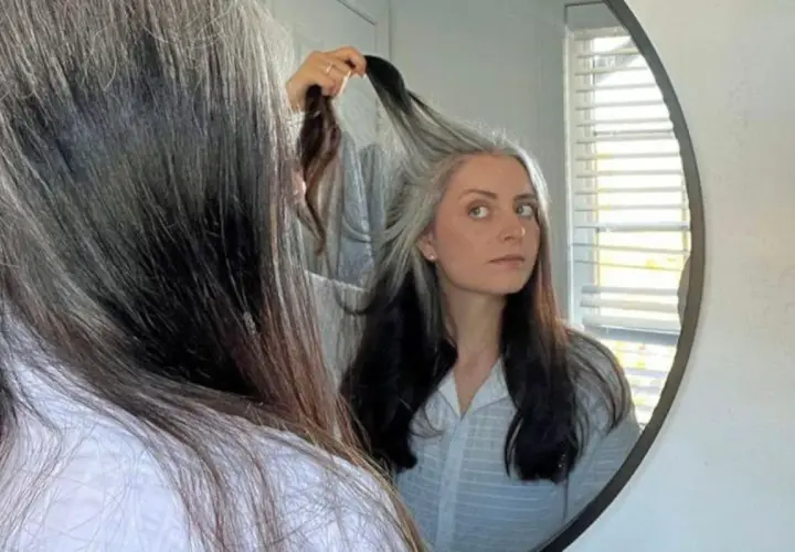 Mujer se mira al espejo, su cabello es una mezcla de negro y canas amarillas, un estilo natural y único.