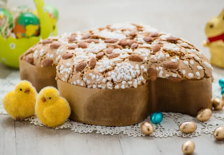 Colomba pasquale, un classico tra i dessert pasquali, decorata con mandorle e zuccherini, circondata da pulcini e uova di cioccolato.