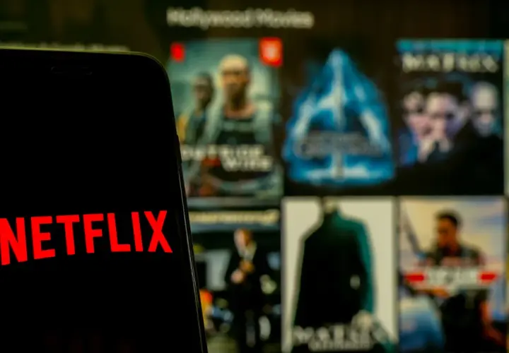 Telefon z logo Netflix na tle ekranu z filmami. Zastanawiasz się, co obejrzeć na Netflixie?