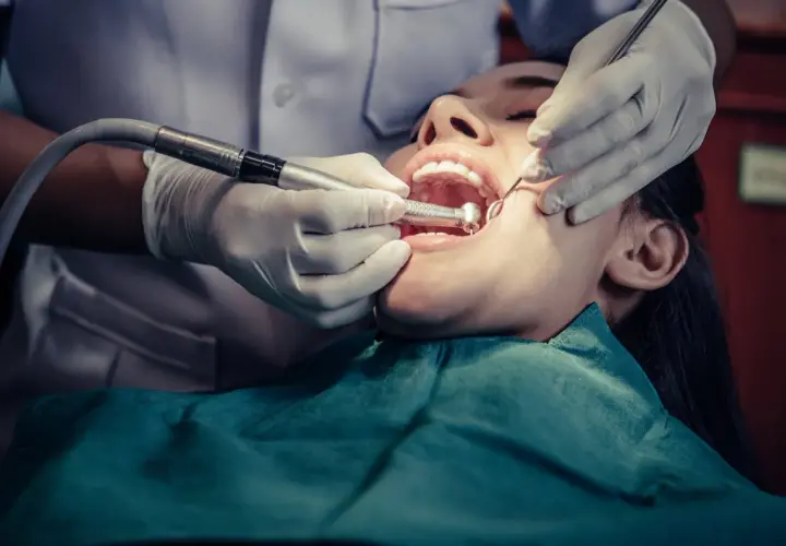 Dentista trabajando en la boca de una paciente, realizando una **conclusión dental** con instrumental y pieza de mano.