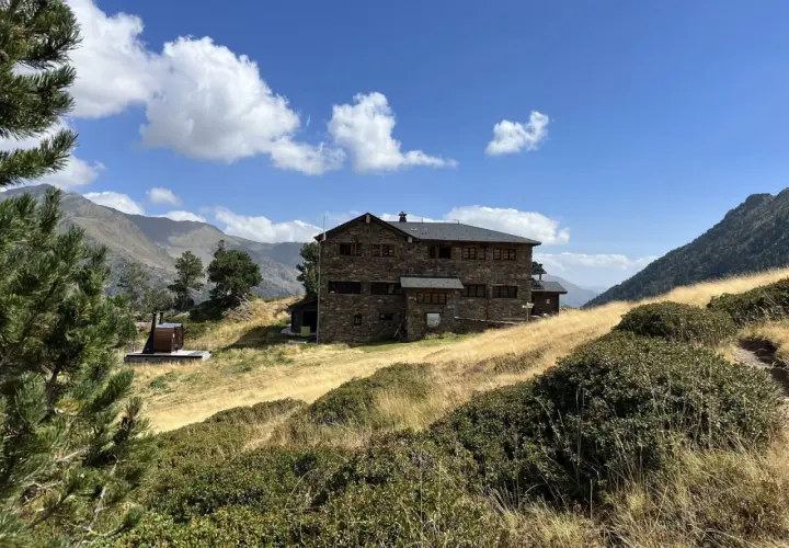 Refugio Comapedrosa, un edificio de piedra en un paisaje montañoso con hierba seca y cielo azul.