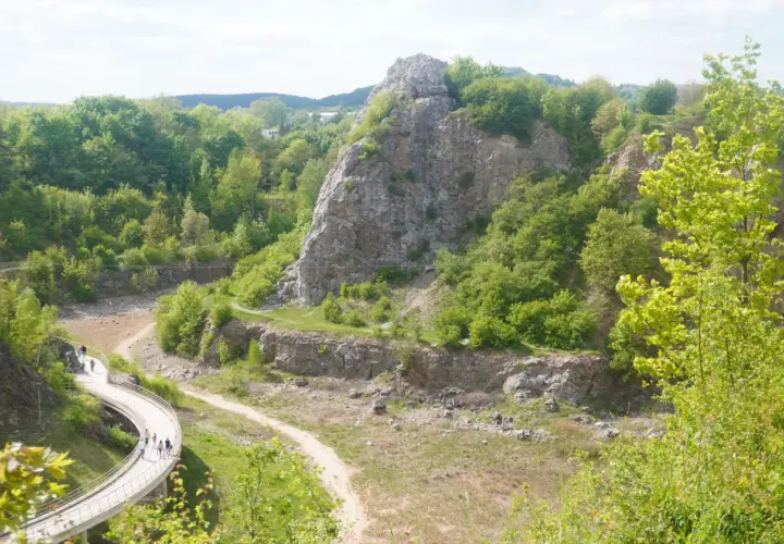 Kamieniołom w Kielcach z krętą ścieżką i grupą spacerowiczów. W oddali skaliste góry porośnięte zielenią.