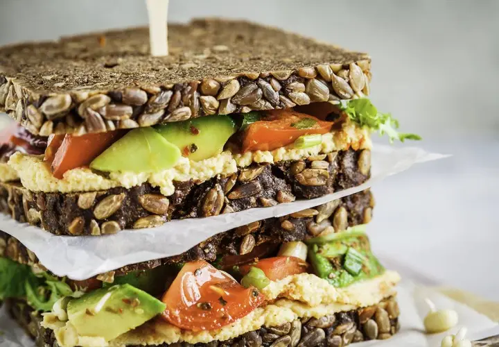 Delicioso sandwich de hummus con aguacate, tomate y pan integral con semillas.