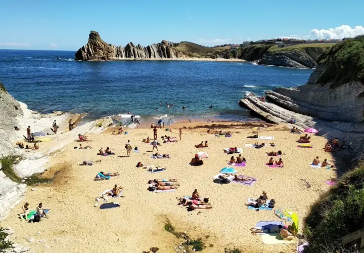 Gente disfrutando del sol y el mar en la playa de cerrias, con formaciones rocosas impresionantes.