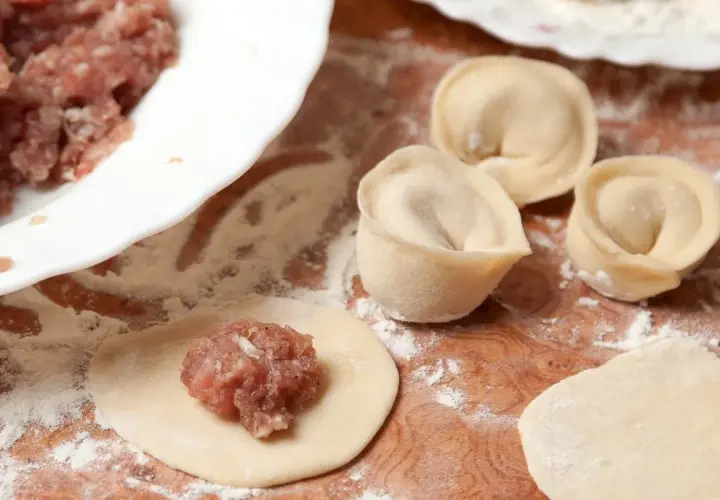 Przygotowanie pierogów: na okrągłym cieście leży farsz na pierogi z mięsem mielonym, obok uformowane pierogi.