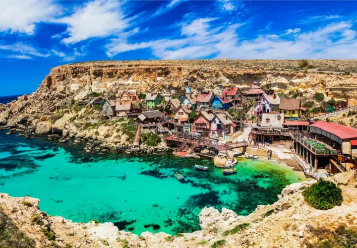 Bunte Häuser am malta beach, umgeben von Felsen und türkisfarbenem Wasser. Boote schaukeln sanft in der Bucht.