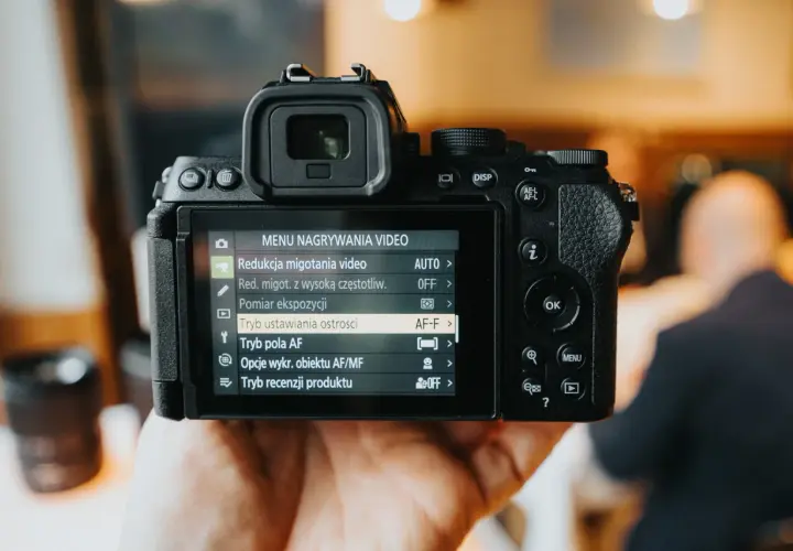 Dłoń trzyma aparat fotograficzny z widocznym menu nagrywania wideo.