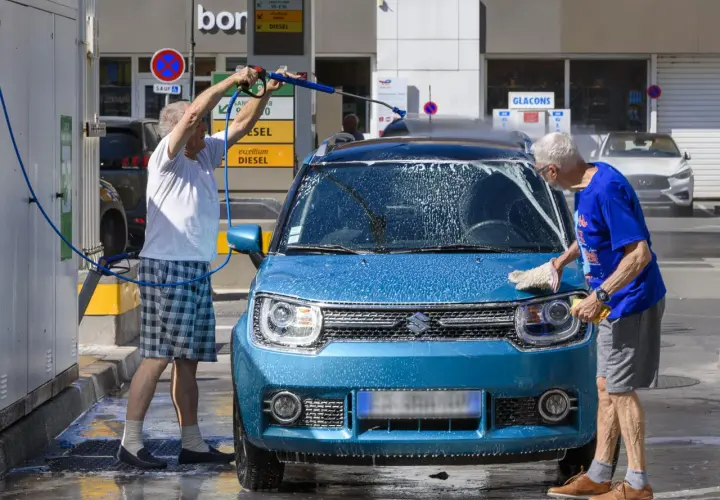 Deux hommes lavent une machine bleue avec de la mousse. L'un utilise un nettoyeur haute pression, l'autre frotte avec une éponge.